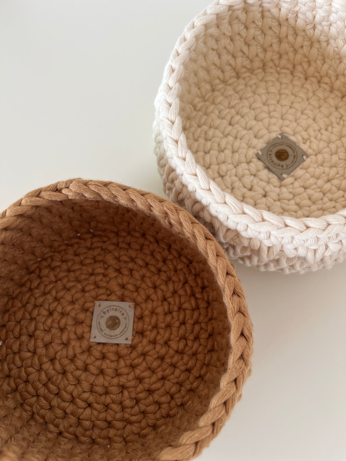 top down view of 2 crochet storage baskets in caramel & cream, showing the byiroiro logo. crochet storage basket, recycled cotton cord, eco friendly storage solution, sustainable homeware, handmade basket, solutions for eco friendly living.