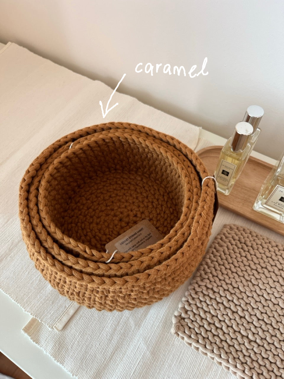 Nested set of 3 handmade crochet baskets in Caramel, placed on a dressing table. crochet storage basket, recycled cotton cord, eco friendly storage solution, sustainable homeware, handmade basket, eco friendly lifestyle solutions.