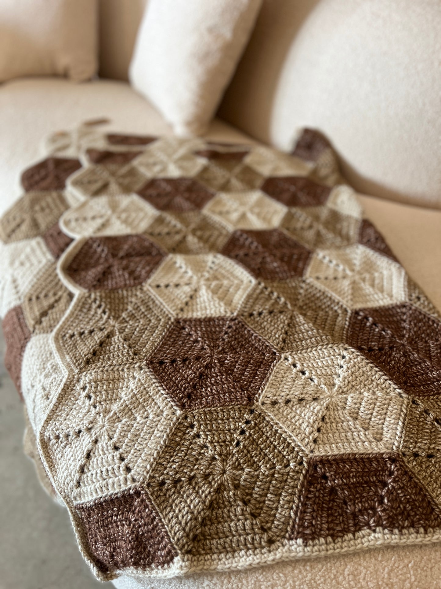 closeup of crochet blanket on a cream boucle sofa, throw blanket, hexagon motifs, cosy warm colours, browns, beiges, handmde, cotton-blend, wool-sensitive