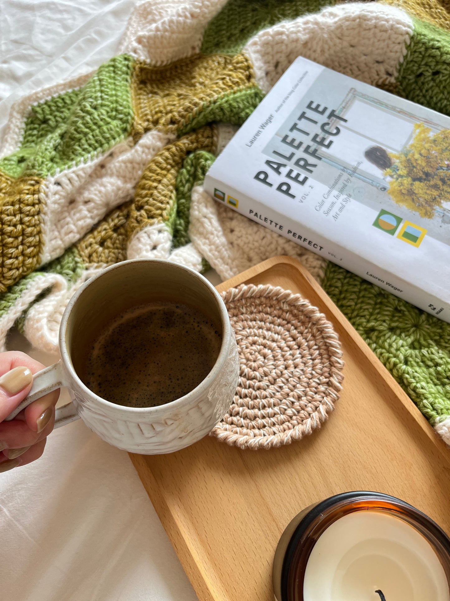 crochet blanket styled on a bed with a book, and a wooden tray with a cup and candle, throw blanket, hexagon motifs, olive green, jasper yellow, handmade, cotton-blend, wool-sensitive, custom throw blanket