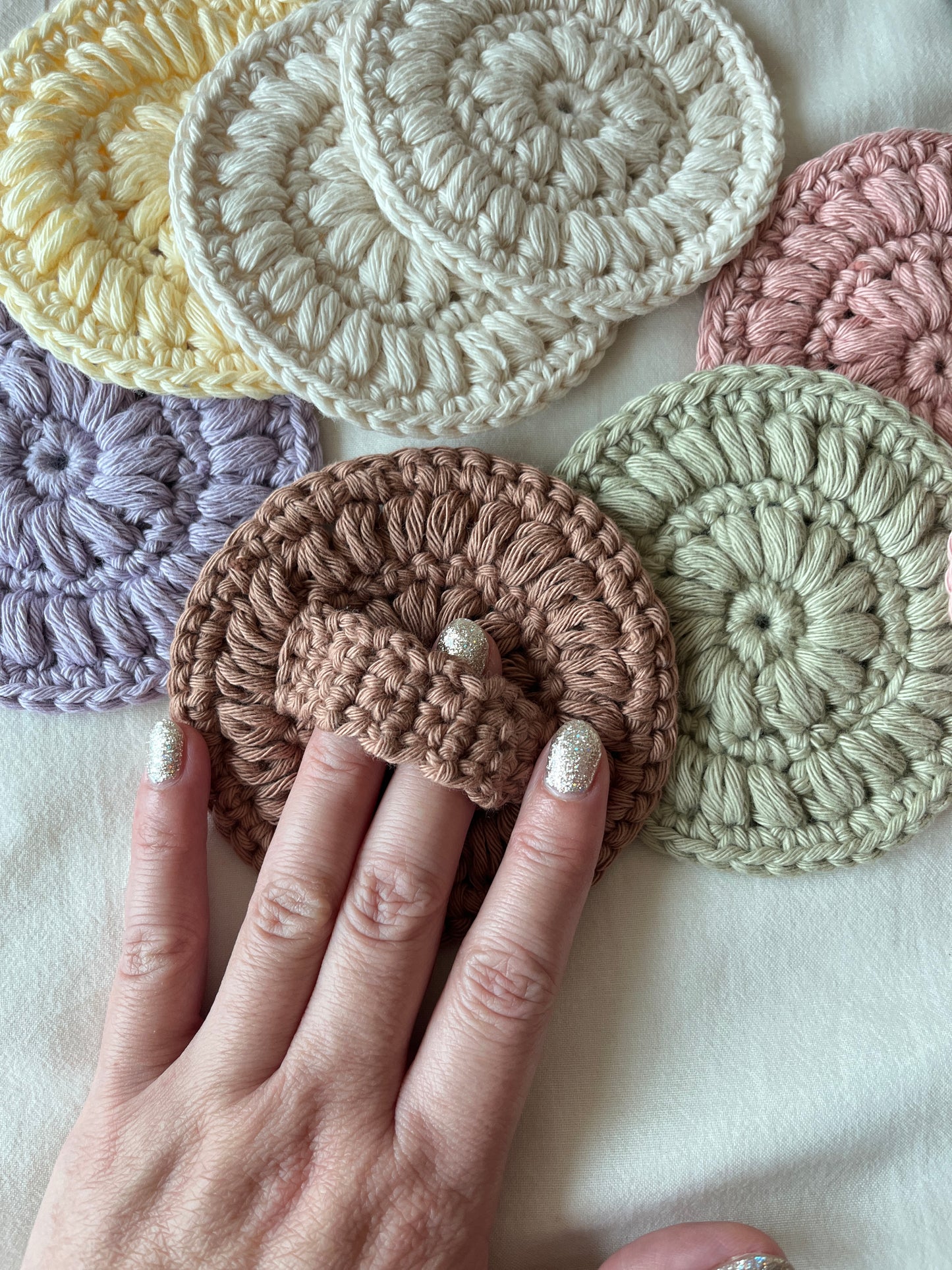 Hand holding a crocheted face scrubby, showing the back with a holding strap