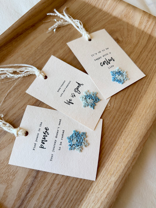 Three affirmation cards, decorated with glittery crochet snowflakes in light blue and white, placed on a wooden tray.
