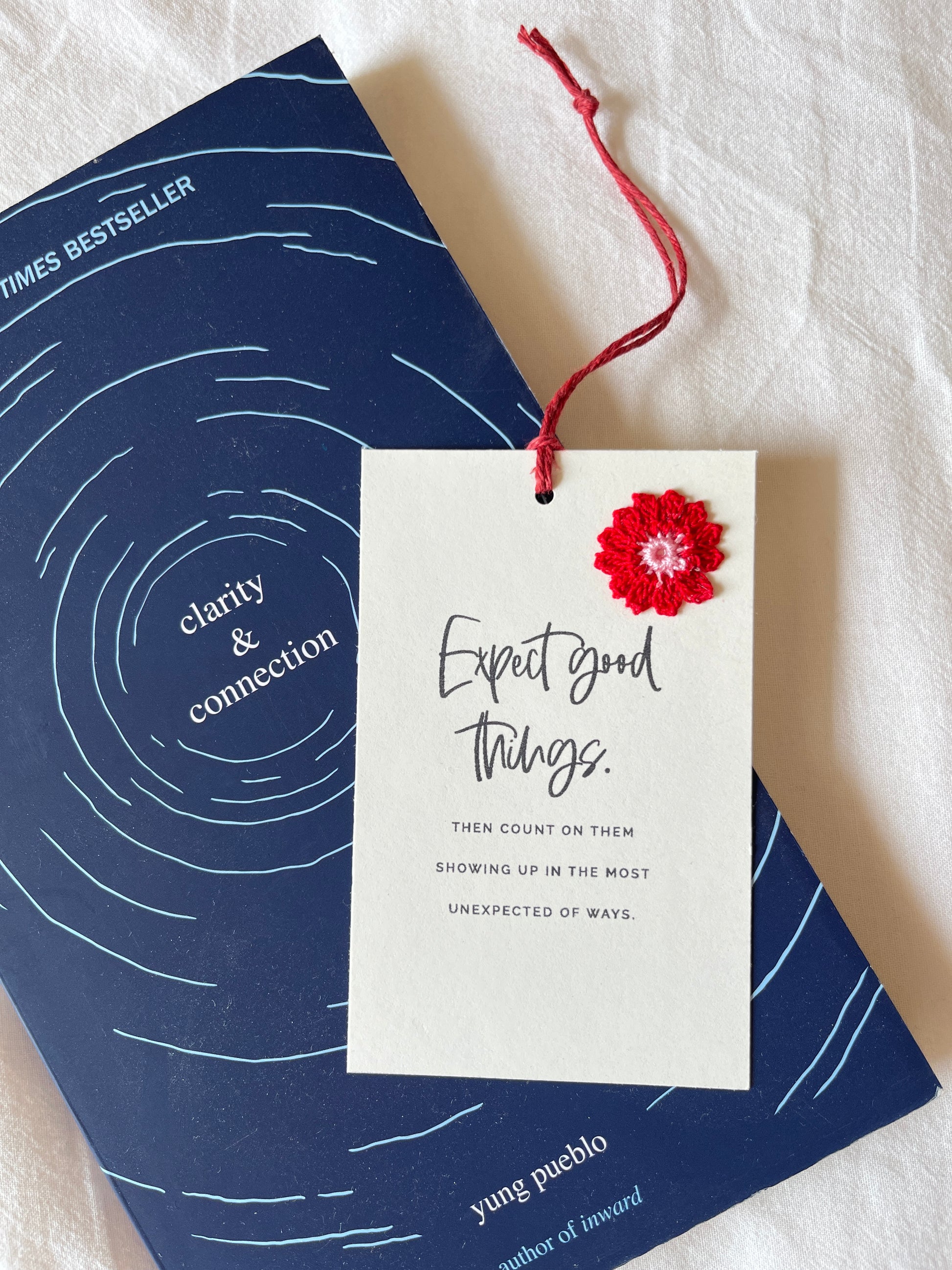 notecard with quote ‘expect good things’ embeliished with a cheerful red crochet flower, placed on top of a book. eco friendly bookmark ideas, sustainable gifting.